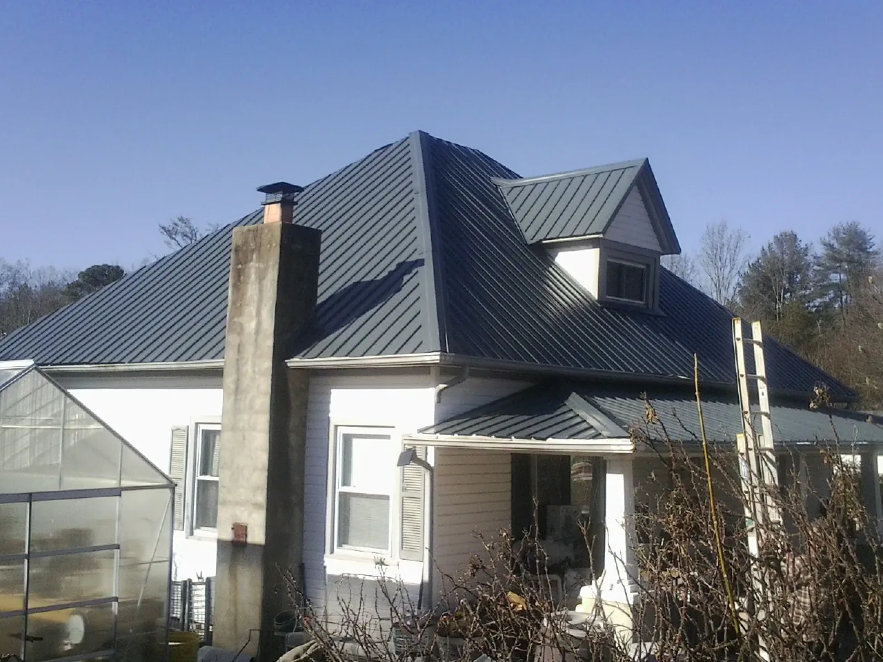 Dark blue standing seam metal roof on a white farmhouse with dormer — Slate & Tile Roof Repair by Roofing Brothers in Farmingdale