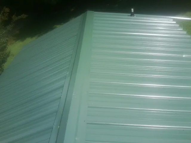 New green metal panels meeting at the ridge of a roof — Flat Roof Repair work by our crew in Farmingdale